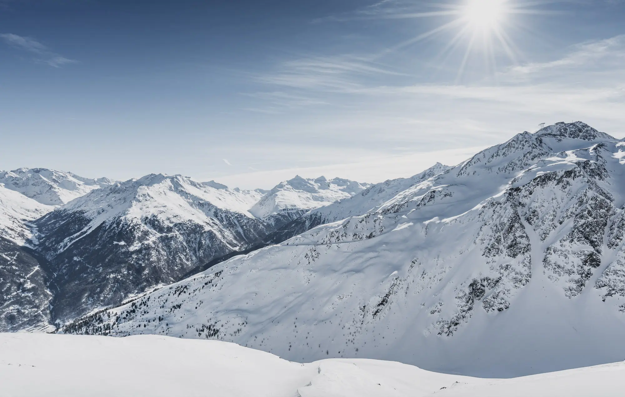 Schneebedeckte Bergkette unter strahlender Sonne und blauem Himmel.