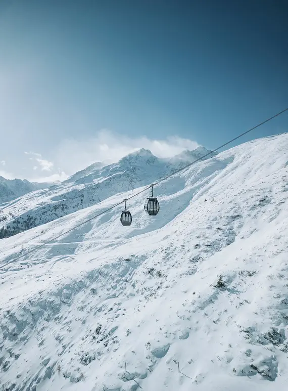 Zwei Skilifte fahren einen verschneiten Berghang hinauf, unter einem klaren blauen Himmel mit fernen Gipfeln im Hintergrund.