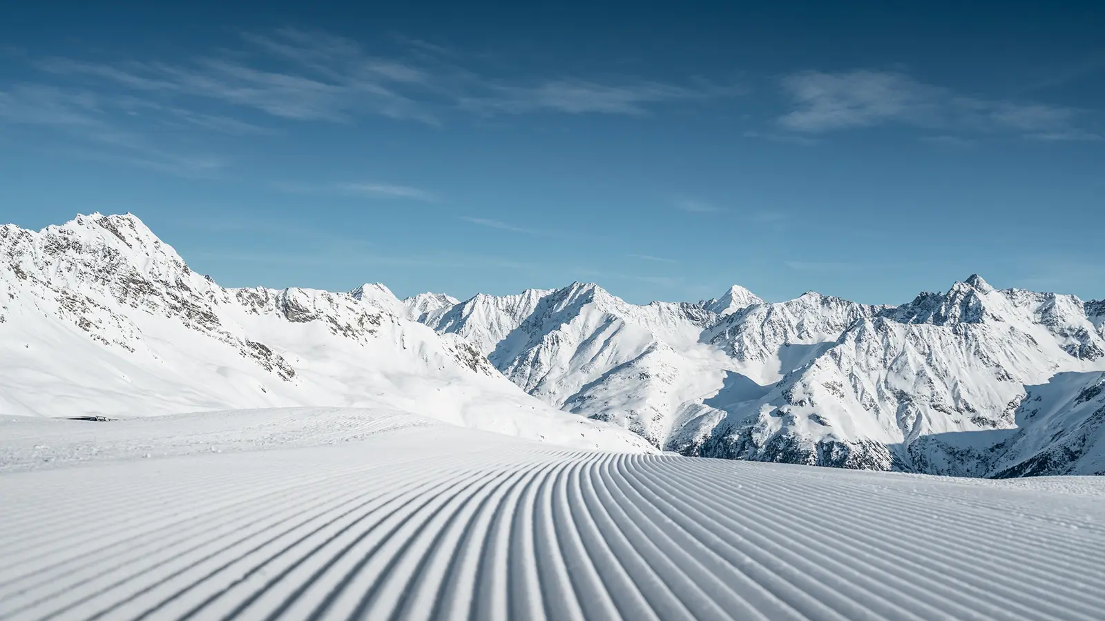 Schneebedeckte Bergkette mit blauem Himmel und sauber präparierten Skipisten im Vordergrund.
