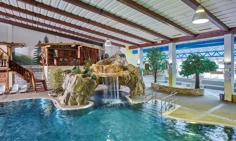 Innenpool mit Felsenwasserfall, Palmen, Wasserrutsche und Wandmalerei einer Strandszene.