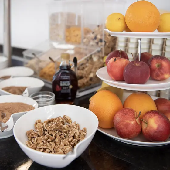 Ein Frühstücksbuffet mit Müsli, Walnüssen, frischen Äpfeln, Orangen und einer Flasche Sirup auf einem Tresen.