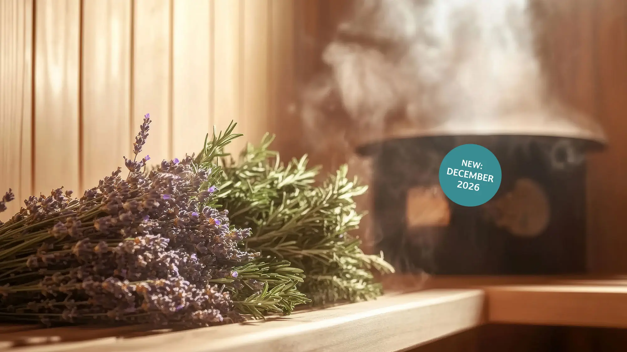 Ein Bündel Lavendel auf einer Holzbank in einer dampfenden Sauna. Türkiser Kreis mit weißer Schrift "New: December 2026" rechts im Bild.