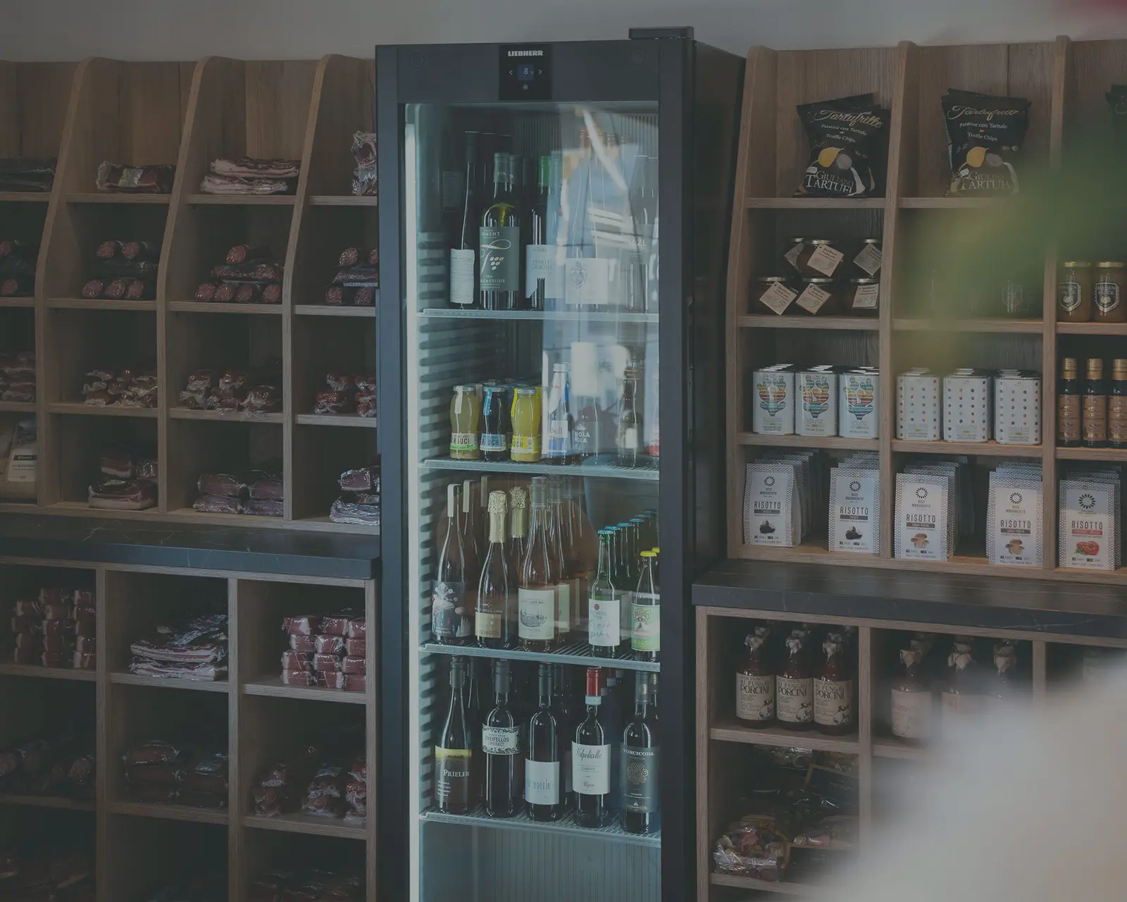 Ein Kühlschrank mit Glastüren und Flaschen, umgeben von Regalen mit verschiedenen verpackten und eingemachten Waren im Alpine Market.