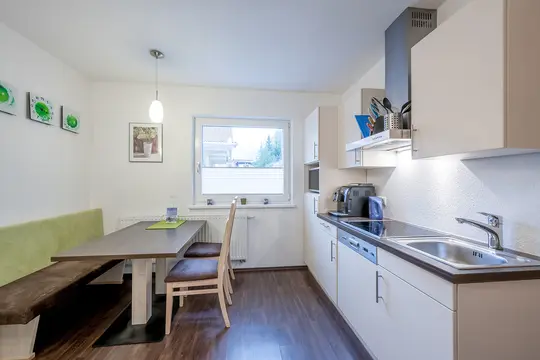 Ein Bündel Lavendel auf einer hölzernen Saunabank, während im Hintergrund Dampf aus einem heißen Ofen aufsteigt.