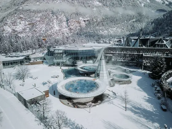 Heiße Quellen des Aqua Dome im Freien, umgeben von schneebedeckten Bergen und Gebäuden in einer Winterlandschaft.