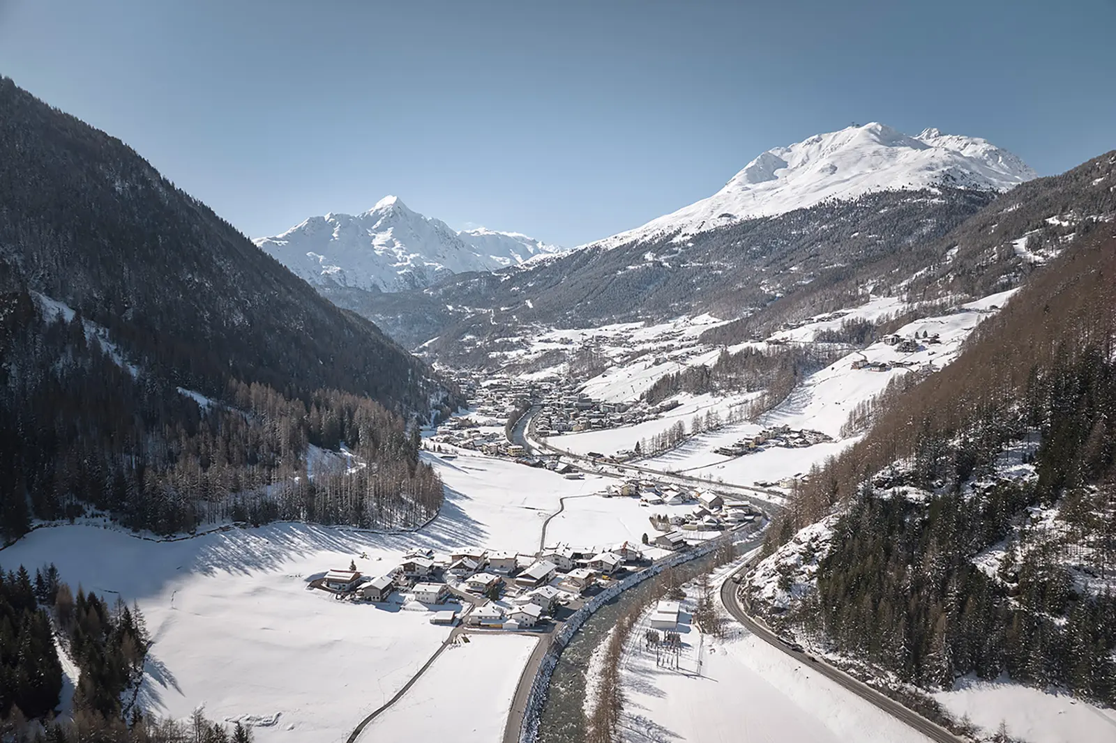 In einem verspiegelten Gebäude spiegeln sich verschneite Berge und Skifahrer unter der strahlenden Sonne eines klaren Wintertages.