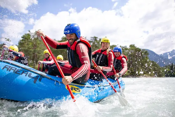 Menschen mit Helmen und Schwimmwesten beim Wildwasser-Rafting, die intensiv paddeln, während das Wasser um sie herum spritzt.