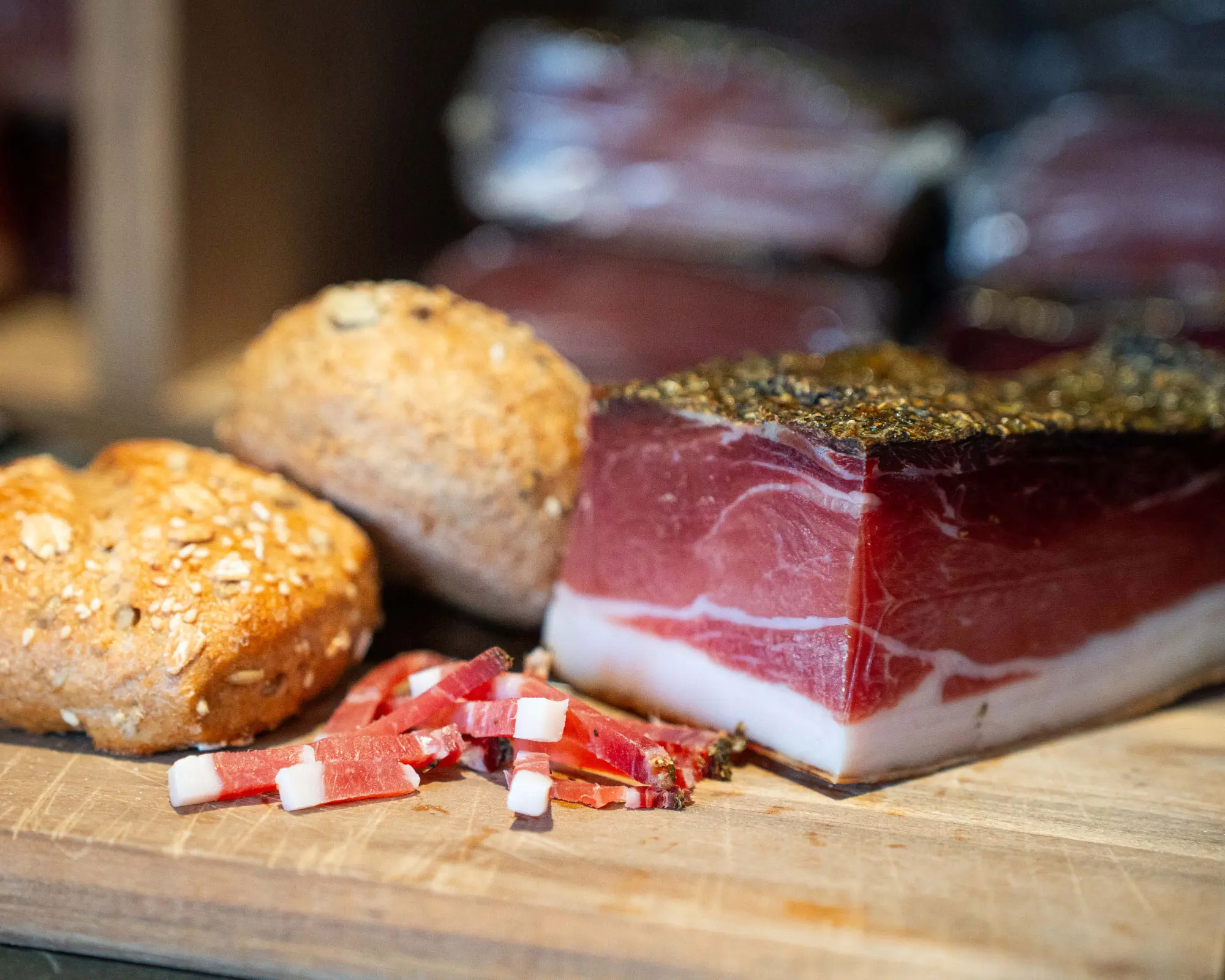 Eine dicke Scheibe Speck und zwei Brötchen auf einer Holzunterlage.