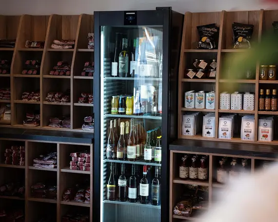 Ein gläserner Kühlschrank mit Flaschen steht zwischen Regalen mit verschiedenen verpackten Waren im Alpine Market.