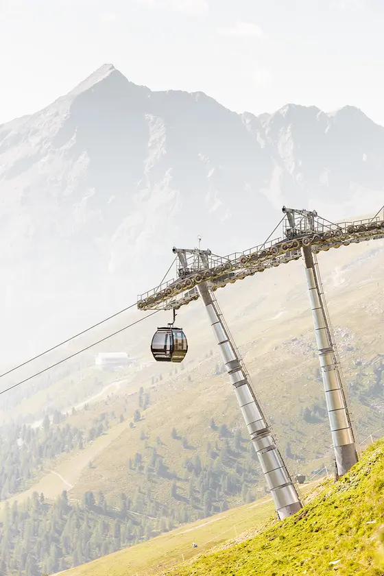Eine Seilbahn fährt auf einen Berg mit einem nebligen Gipfel und grünen Hängen im Hintergrund.